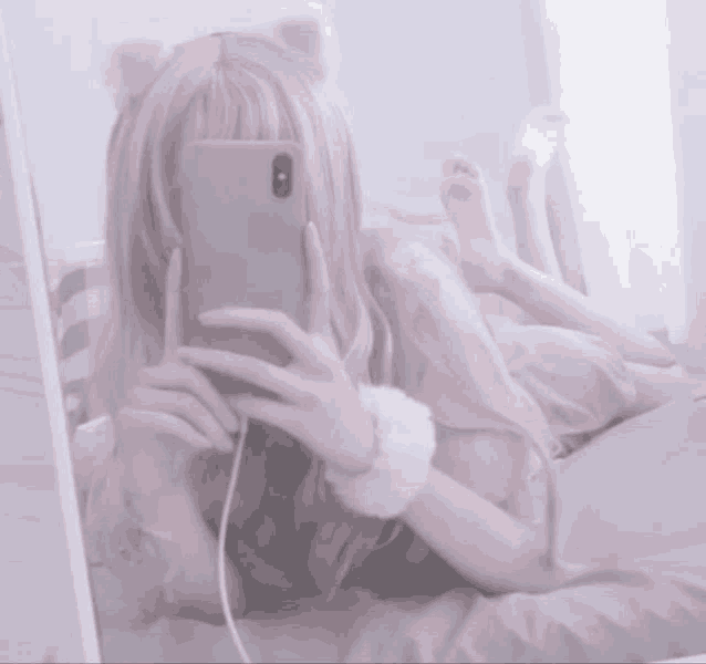 a girl with cat ears is taking a picture of herself in the mirror with her phone .