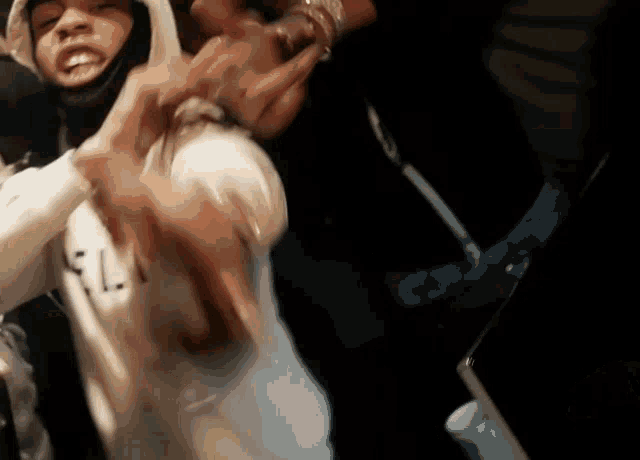 a man in a white hoodie is standing in a crowd with his hands in his pockets .