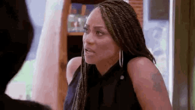 a woman with braids is making a funny face while talking to another woman .