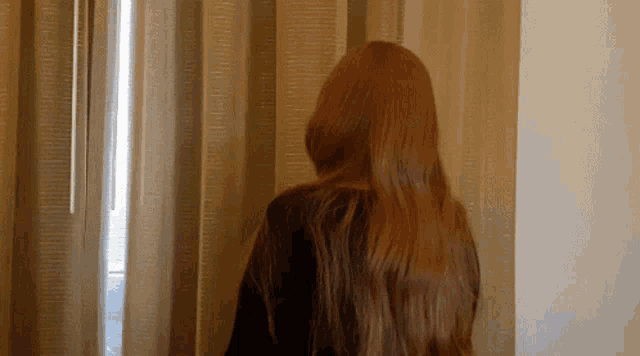 a woman with very long red hair stands in front of a window