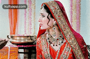 a woman in a red and gold wedding dress is sitting next to a man in a bowl .