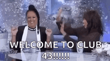 two women are sitting at a table with their arms in the air and a sign that says `` welcome to club 43 '' .