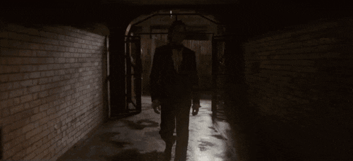 a man in a suit and tie walks through a dark hallway
