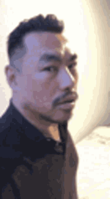 a man with a beard is standing in front of a white wall and looking at the camera .