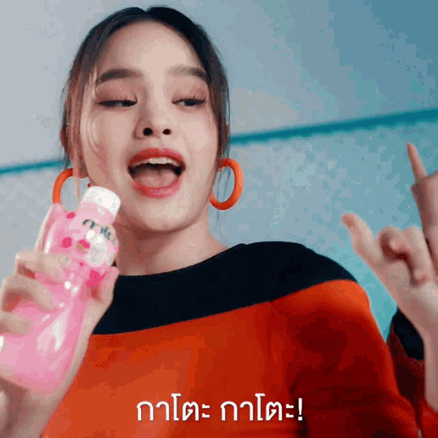 a woman is holding a pink bottle with a foreign language on the bottom right