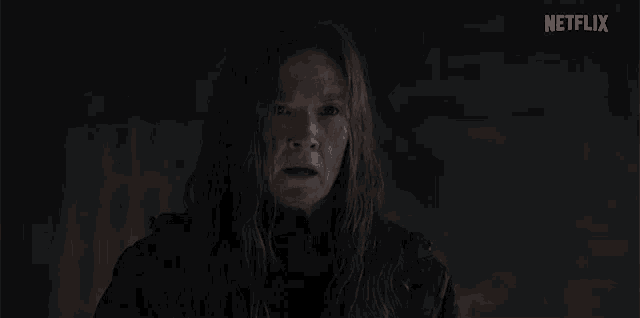 a woman with long hair is standing in the dark and looking at the camera .
