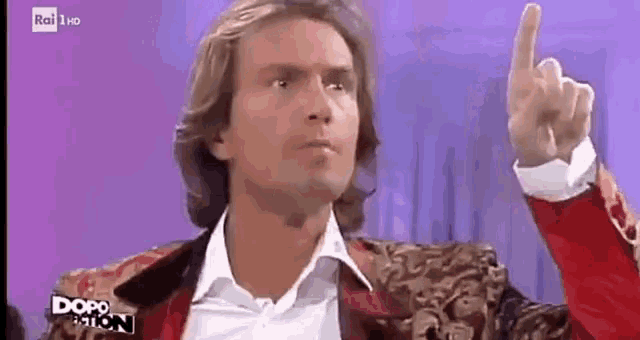 a man in a red jacket is pointing his finger up .
