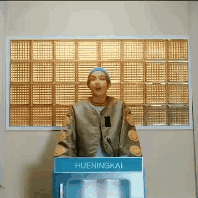 a man is standing in front of a blue box that says hueningkai