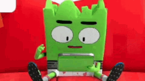 a green cartoon character is sitting on a red couch and using a tablet .