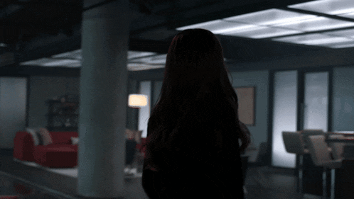 a woman is standing in a dark room with a red couch