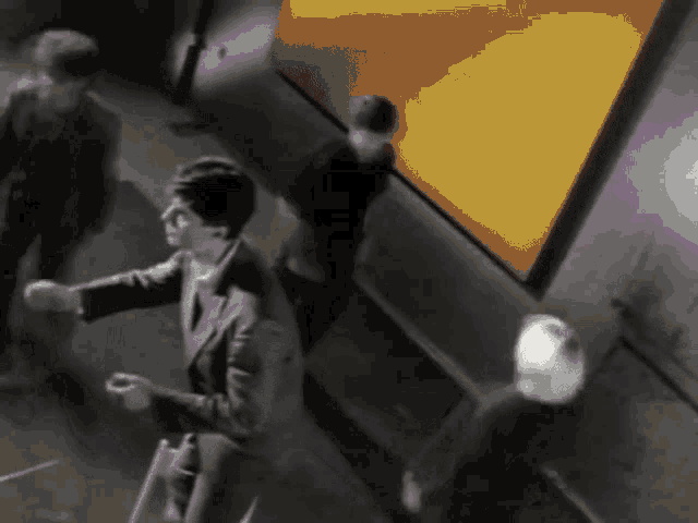 a black and white photo of people walking in a hallway with a yellow wall in the background