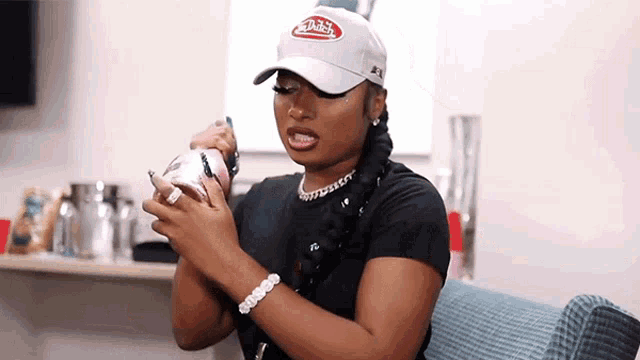 a woman wearing a hat and a bracelet is sitting on a chair holding a cell phone .