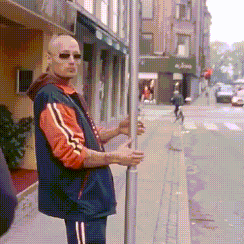 a man in an orange and blue jacket is standing on a sidewalk holding onto a pole