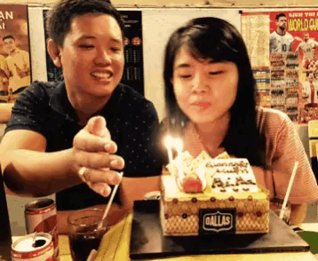 a man and woman blowing out candles on a dallas birthday cake