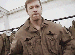 a man wearing a brown jacket is standing in front of a rack of clothes
