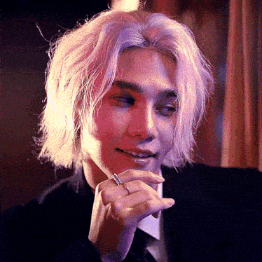 a man with long blonde hair and a ring on his finger looks at the camera