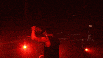 a man in a black tank top is singing into a microphone in a dark room