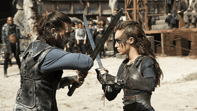 a man and a woman are fighting with swords on a sandy field