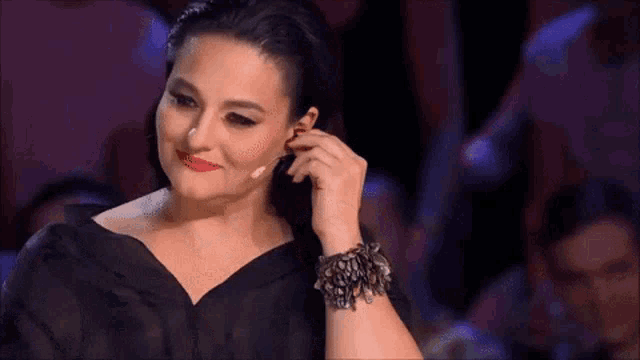 a woman in a black dress is adjusting her earring while wearing a bracelet .