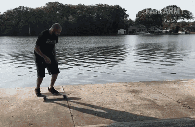 a man wearing a shirt that says infinity is riding a skateboard near a body of water