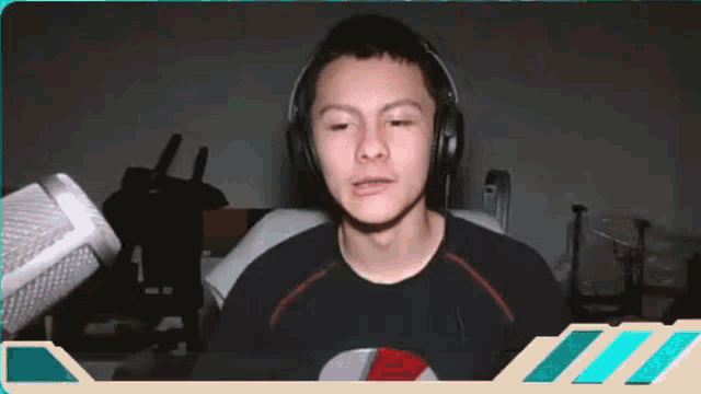 a young man wearing headphones and a black shirt is sitting in front of a microphone .