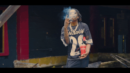 a man wearing a black shirt with the number 24 on it smoking a cigarette
