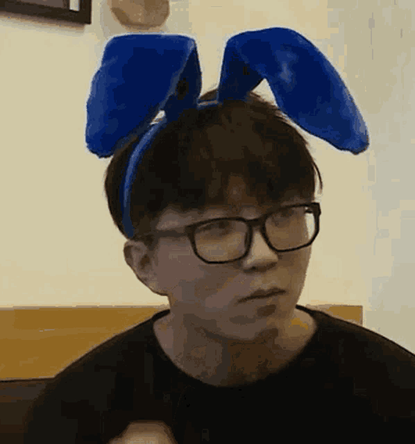 a man wearing glasses and blue bunny ears is sitting in a chair .