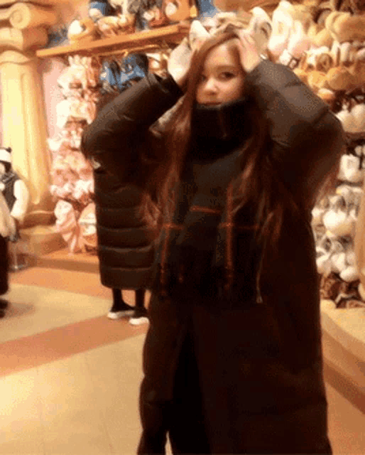 a woman in a black coat holds her hands to her head in front of a stuffed animal display