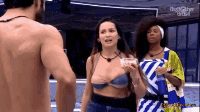 a man and two women are standing next to each other in a room . the woman is wearing a bikini top .