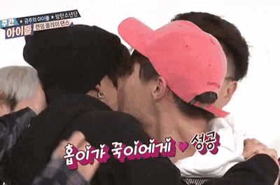 a man in a pink hat is kissing another man in a black hat