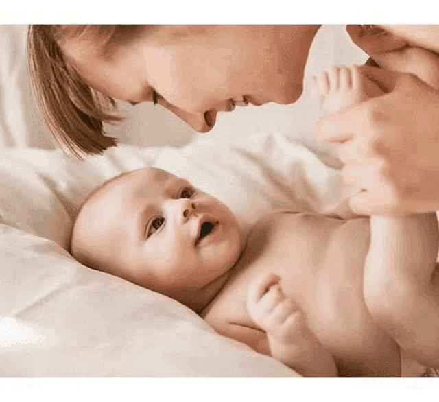 a woman is touching a baby 's foot while the baby is laying on a bed .