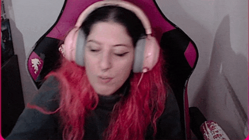 a woman with red hair is sitting in a pink chair wearing headphones .