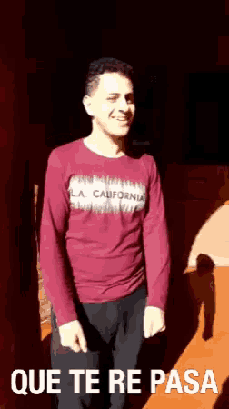 a man wearing a la california shirt is standing in front of a wall