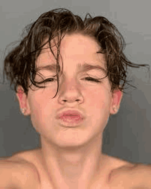a young boy without a shirt is making a funny face with his eyes closed .