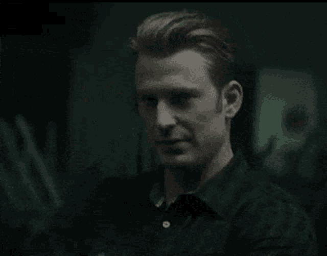 a man in a black shirt is standing in a dark room and looking at something .