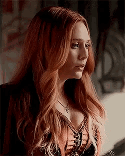 a woman with long red hair is wearing a necklace and a lace up top .