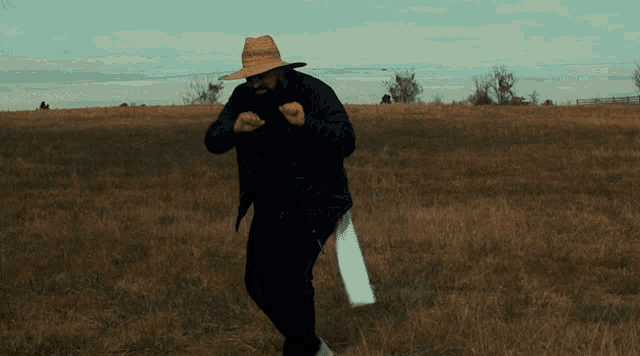a man wearing a straw hat and a black jacket is dancing in a field