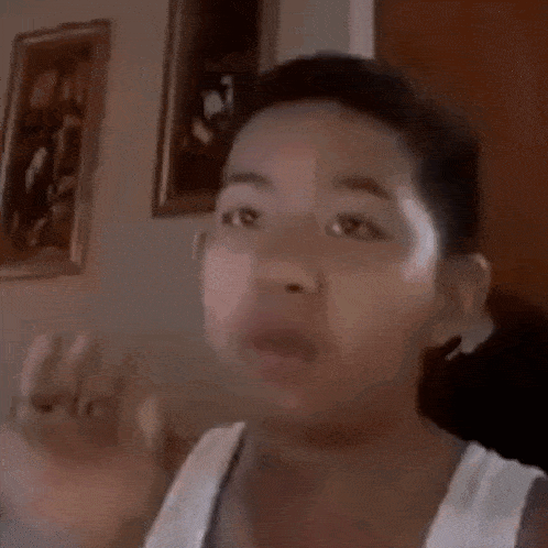 a young boy in a white tank top is making a funny face in a room .
