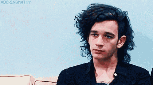 a young man with long black hair is sitting on a couch with his eyes closed .