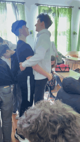 a man in a white hoodie holds another man in his arms in a room