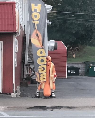 a statue of a hot dog stands in front of a sign that says hot dogs