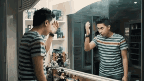 a man in a striped shirt is looking at his reflection in a mirror
