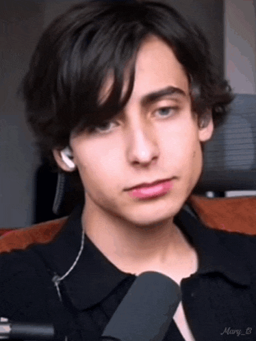 a young man wearing headphones and a tie is sitting on a couch and looking at the camera .
