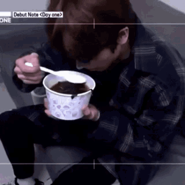 a man is sitting on the floor eating a bowl of soup with a spoon and the words debut note day one on the bottom