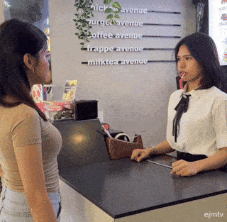 a woman is talking to another woman at a counter in front of a sign that says milktea avenue