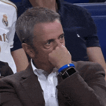 a man in a suit covering his mouth with his hand while wearing a blue watch