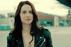 a woman in a leather jacket is standing in a parking lot looking at the camera .