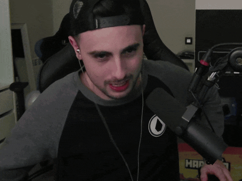 a man wearing headphones and a hat stands in front of a microphone in front of a wall that says mafia