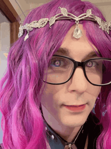 a man with pink hair and glasses is wearing a tiara on his head