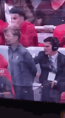 a man in a suit and tie is standing next to another man in a stadium .